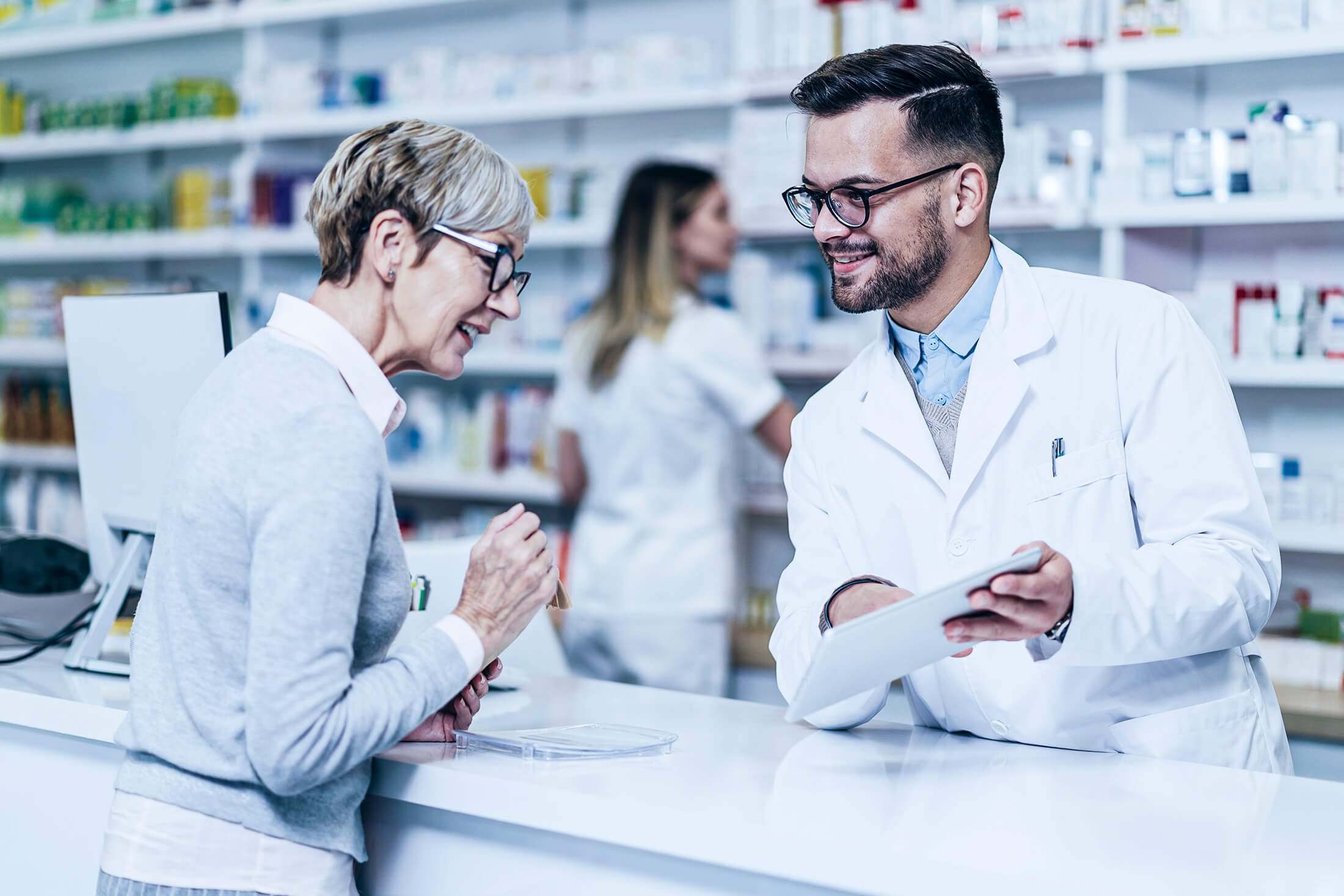 Qual o melhor horário de funcionamento da farmácia? Na imagem, uma senhora é atendida por um farmacêutico.